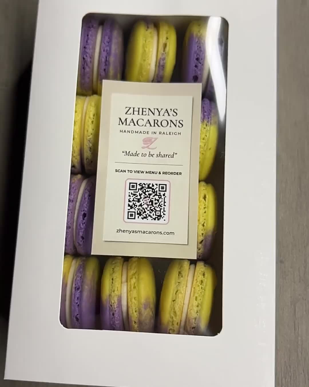 A white window gift box of purple and yellow macarons from Zhenya's Macarons, handmade in Raleigh